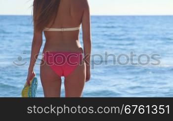 Girl in pink bikini with flip flops at the summer beach