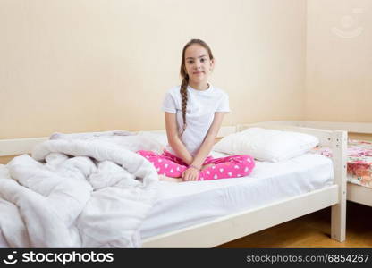 Girl in pink pajamas sitting on bed with white sheets and blanket