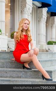 girl in red dress with beautiful curls sitting on the steps