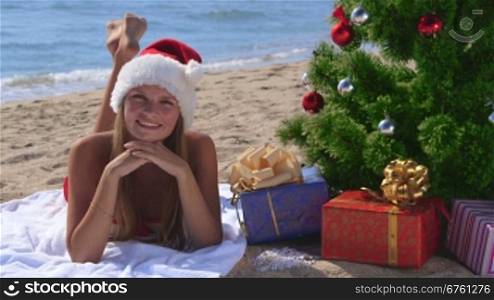 Girl in Santa hat celebrating Christmas on tropical beach looking at the camera smiling