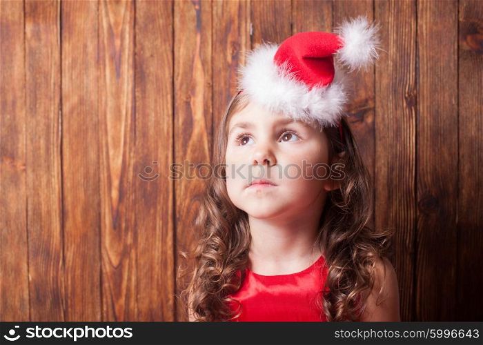 Girl in Santa hat headband sitting over wooden wall, copy space