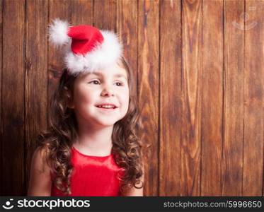 Girl in Santa hat headband sitting over wooden wall, copy space
