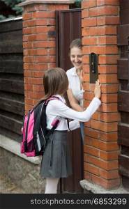 Girl in school uniform ringing in doorbell and mother opening the door