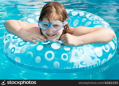 girl in swim goggle on swimming circle in blue open-air pool