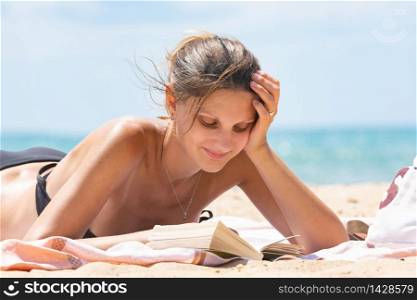 Girl in swimsuit reads book lying on sandy beach near the sea