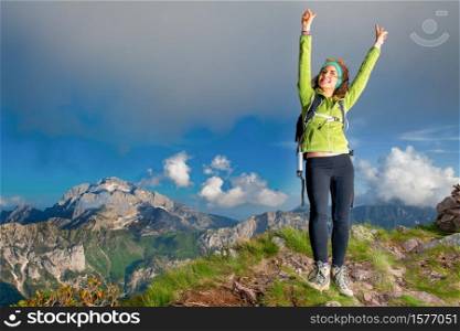 Girl in the summit at the mountain raises her arms happy.