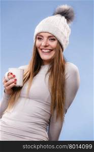 girl in thermal underwear drinking tea. Woman in winter cap gray sports thermal underwear for skiing training holds mug with tea or coffee warming herself studio shot on blue.
