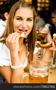 Girl in traditional Dirndl dress is drinking beer and eating a Bretzel while having fun at the Oktoberfest. Girl drinking beer at Oktoberfest