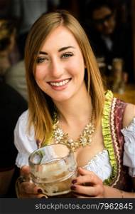 Girl in traditional Dirndl dress is drinking beer while having fun at the Oktoberfest. Girl drinking beer at Oktoberfest