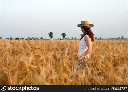 Girl in wheat field in white dress and stetson hat. Selective focus.