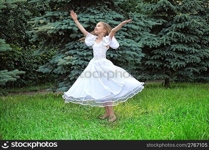 girl in white dress dances on lawn with lifted hands