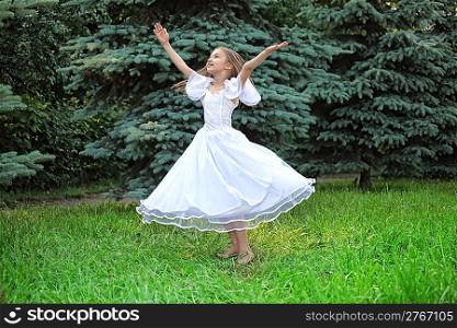 girl in white dress dances on lawn with lifted hands