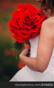 girl in white wedding dress with red flowers in her hands. in the background of red flowers. summer. girl in white wedding dress with red flowers in her hands. in the background of red flowers