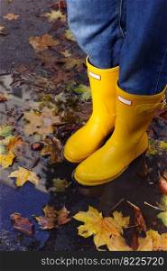 girl in yellow rubber boots stands in a puddle 