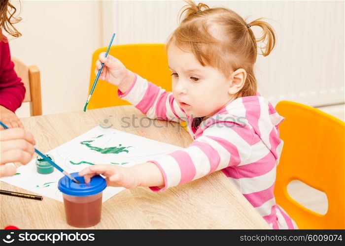 Girl is painting with a brush and watercolors on paper in the kindergarten. Girl is painting