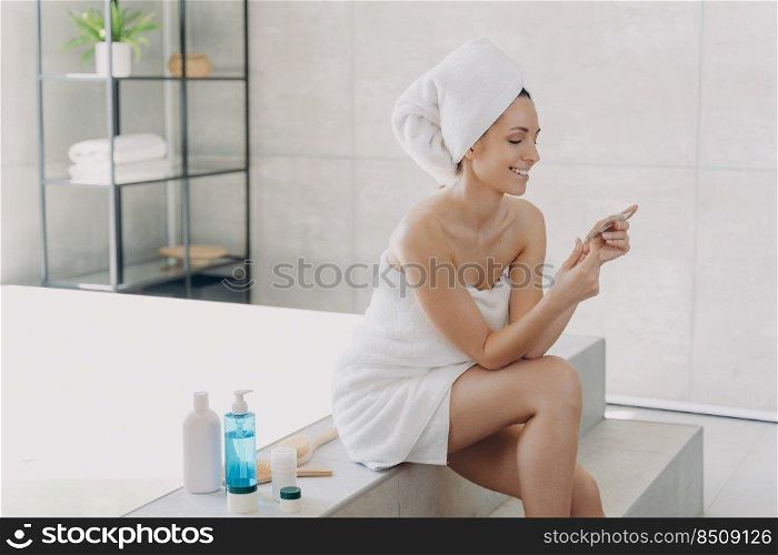 Girl is reading cosmetics ingredients list on the pack and smiling. Gorgeous european woman wrapped in towel after bathing. Young lady at spa resort. Concept of natural cosmetics and wellness.. Girl is reading cosmetics ingredients list on the pack and smiling. Concept of natural cosmetics.