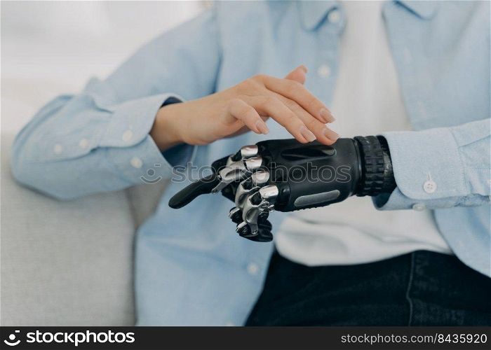 Girl is setting up her bionic hand and pressing buttons. Young european woman with black artificial arm at home. Modern bionic prosthesis. Healthcare technology and innovation concept.. Girl is setting up her bionic hand and pressing buttons. Young woman with artificial arm at home.