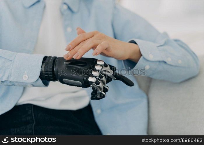 Girl is setting up her bionic hand and pressing buttons. Young european woman with black artificial arm at home. Modern bionic prosthesis. Healthcare technology and innovation concept.. Girl is setting up her bionic hand and pressing buttons. Young woman with artificial arm at home.