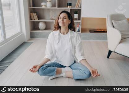 Girl is sitting in lotus pose with her eyes closed. Happy european woman is practicing yoga and meditation on floor at home. Morning gymnastics and zen. Stress relief, wellbeing and peace concept.. Girl is sitting in lotus pose with her eyes closed. Stress relief, wellbeing and peace concept.