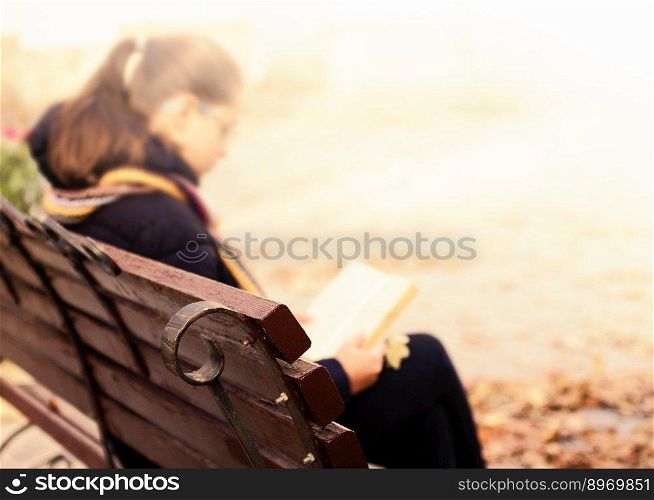 Girl is sitting on bench and reading book.