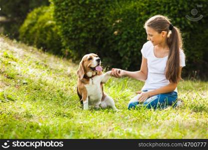 Girl is sitting with beagle dog on the grass. Girl plays with a dog