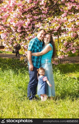 Girl is standing near mother and father against the backdrop of sakura blossoms. Happy family outdoor