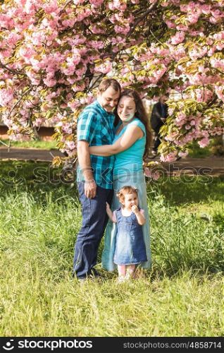 Girl is standing near mother and father against the backdrop of sakura blossoms. Happy family outdoor