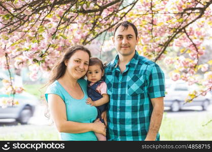 Girl is standing near mother and father against the backdrop of sakura blossoms. Happy family outdoor