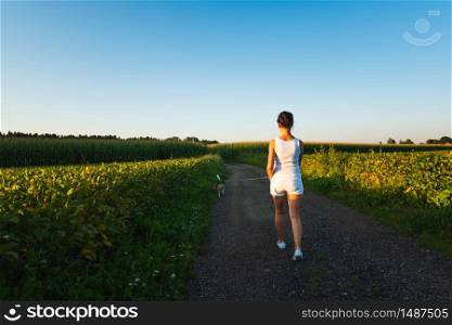 Girl is walking with a beagle dog on a leash in the sunset to the forest in rural area. Pet care. Girl is walking with a beagle dog on a leash in the sunset to the forest in rural area.
