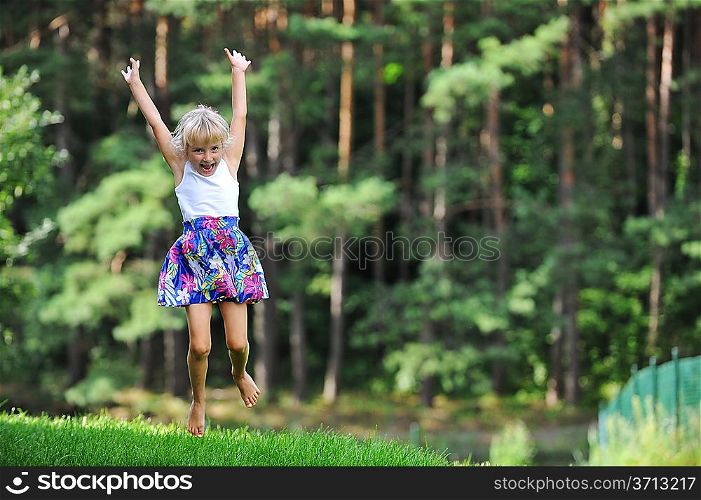 girl jumping on green lawn. Behind her is seen pine forest