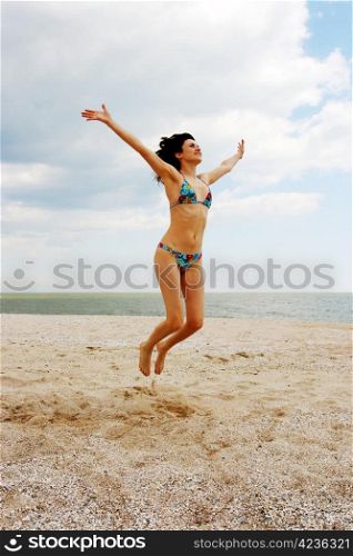 Girl jumping on the beach on the background of the sea and cloudy sky