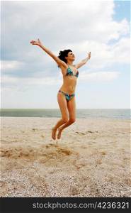 Girl jumping on the beach on the background of the sea and cloudy sky