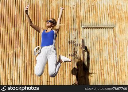 Girl jumping while making a selfie with her smartphone with a rusty metal door in the background.. Girl jumping while making a selfie with her smartphone.