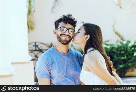Girl kissing her boyfriend on the cheek while smiling. Young woman kissing her boyfriend on the cheek in the street. Concept of happy girlfriend kissing cheek of her boyfriend outdoors