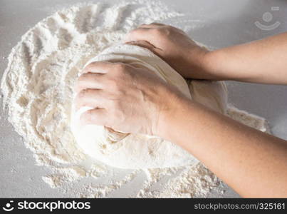 Girl kneads dough on a white table close-up.