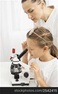girl learning look into microscope with female teacher