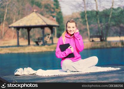 Girl learning yoga from tablet.. Young girl sitting in park learning yoga from tablet covering body. Taking care about healthy lifestyle and slim figure. Sport with technology.