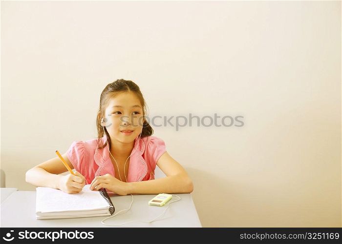 Girl listening to an MP3 player and holding a pen on a spiral notebook
