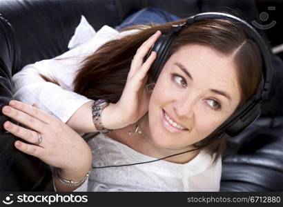 girl listening to music on her headphones at home lying on a black leather sofa