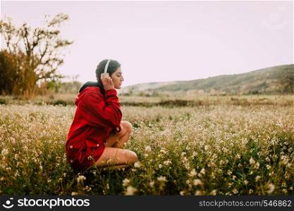 Girl listening to music with headphones sitting among wildflowers