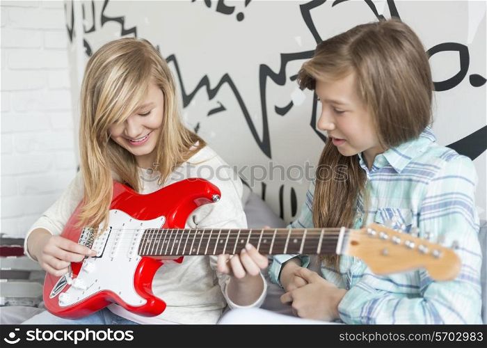 Girl listening to sister playing electric guitar at home