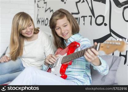 Girl listening to sister playing guitar at home