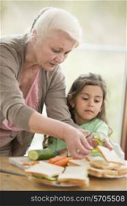 Girl looking at grandmother preparing sandwiches at home