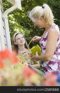 Girl looking at her grandmother watering flowers