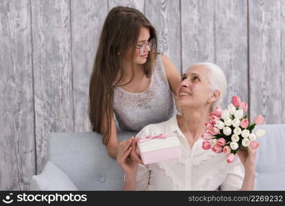 girl looking her grandmother holding gift box tulip flower bouquet hands