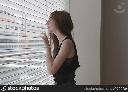 Girl looking through slatted blinds