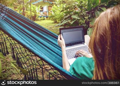 girl lying in a hammock and working on a laptop at the garden