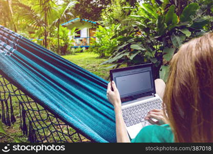 girl lying in a hammock and working on a laptop at the garden