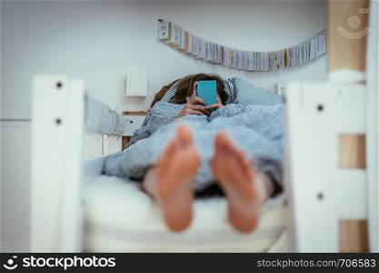 Girl lying in bed is using her smartphone, smartphone in the foreground, blurry background