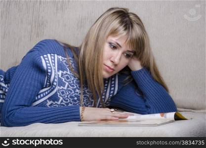 Girl lying on the couch and reading a book. A girl dressed in a warm sweater and covered her warm blanket